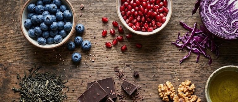 Продукты, богатые полифенолами: ягоды, гранат, зелёный чай и оливковое масло на деревянном столе